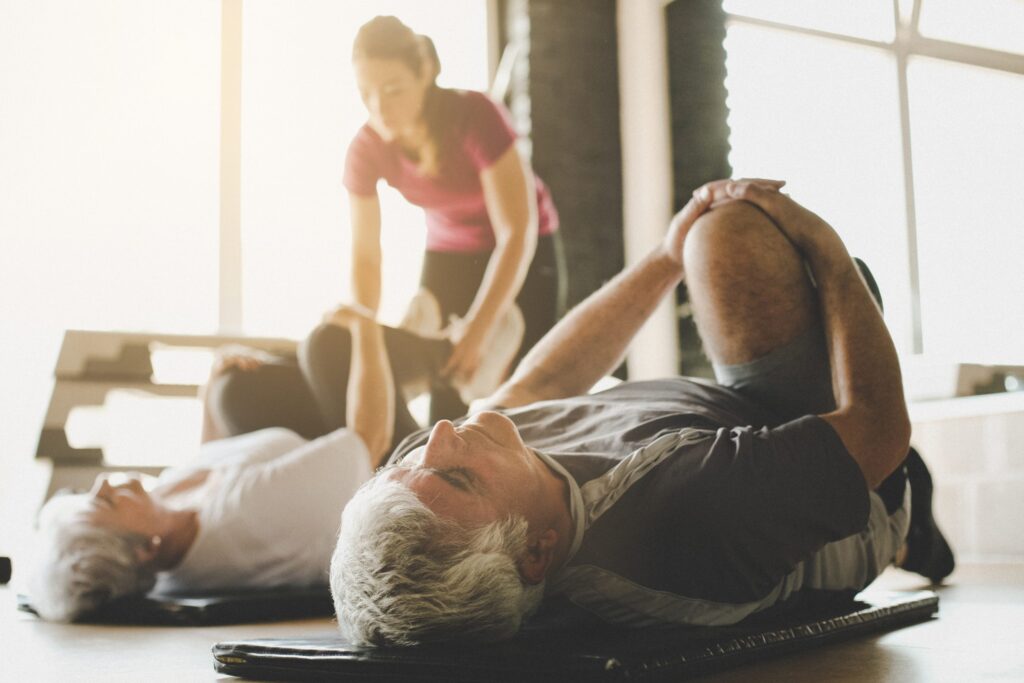 senior-couple-workout-in-rehabilitation-center.-personal-trainer-helps-elderly-couple-to-do-stretching-on-the-floor.-focus-on-man.-687027214_4368x2912-scaled-1-1024x683.jpeg